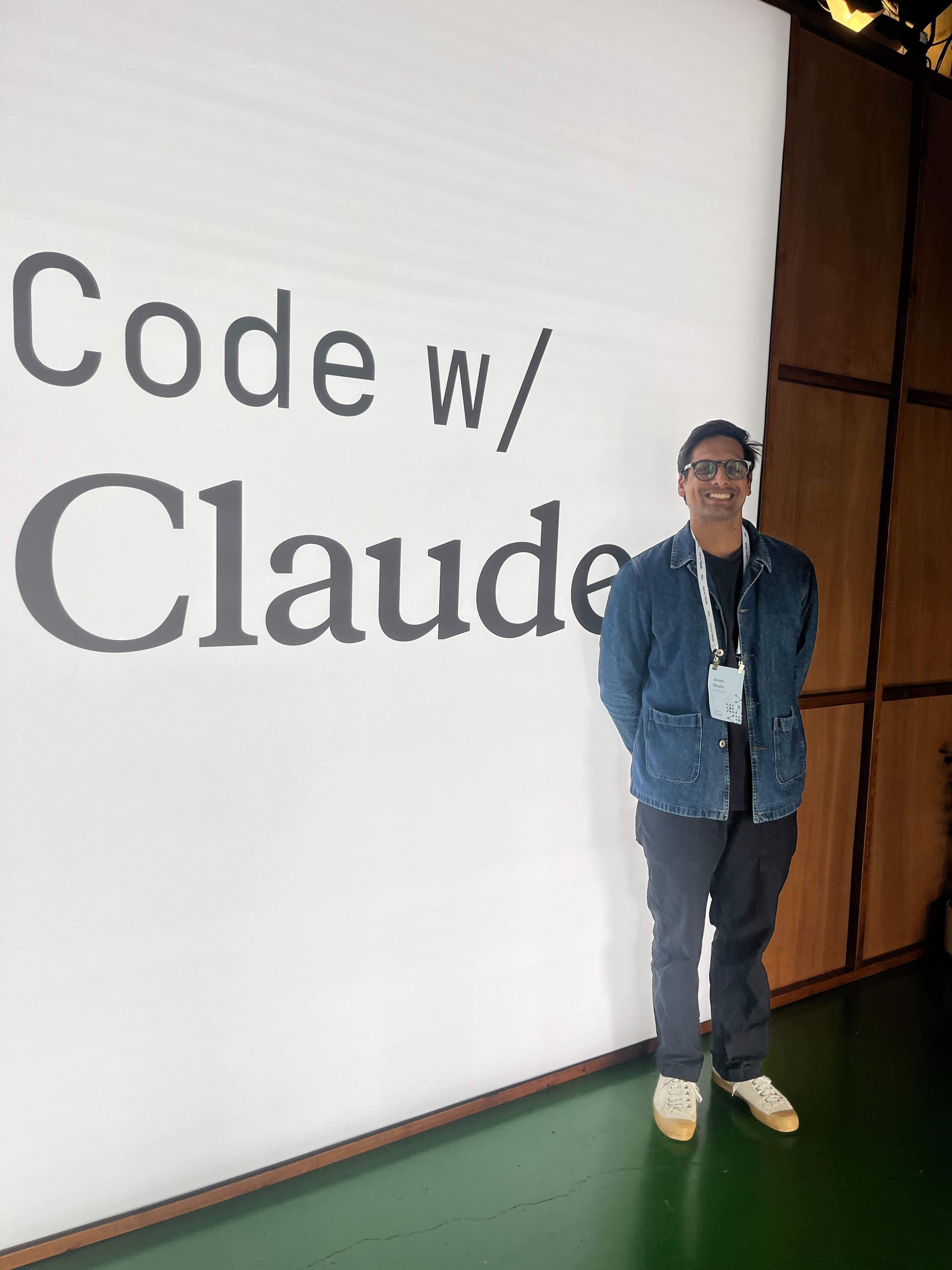 Areeb standing in front of the large 'Code w/ Claude' wall at the event
